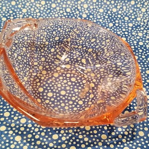 May include: A pink glass bowl with two handles. The bowl has a textured surface with small white dots.