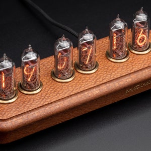 Op de afbeelding: Een houten klok met zes gloeiende Nixie-buizen die de tijd 19:77:16 weergeven. De klok is gemaakt van donker hout met een lederachtige textuur en heeft de inscriptie "NixieClock" aan de zijkant.