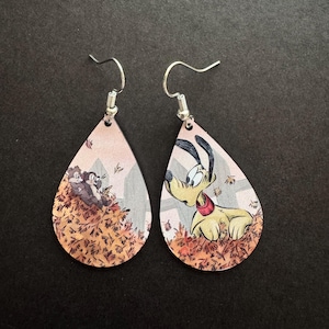 May include: Teardrop-shaped dangle earrings featuring a printed illustration of two chipmunks in a pile of autumn leaves on one earring and a yellow dog with a red collar in a pile of autumn leaves on the other, with silver-toned metal hooks.
