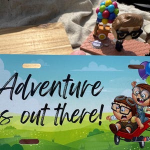 May include: A license plate with the phrase "Adventure is out there!" in black script over a cartoon scene of two children in a red wagon. The background is a green field and blue sky.