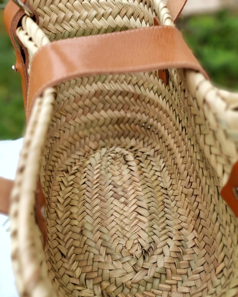 May include: A woven straw bag with a brown leather handle. The bag is open and the inside is visible. The straw is woven in a herringbone pattern.