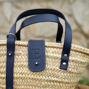 May include: A woven straw basket with black leather handles and a black leather patch with the letter "E" embossed on it.