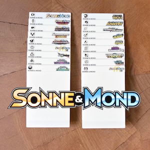 Peut inclure: Deux s&eacute;parateurs en plastique blanc rectangulaires pour le rangement de cartes &agrave; collectionner, chacun pr&eacute;sentant une colonne d'&eacute;tiquettes imprim&eacute;es avec le texte Sonne & Mond, divers logos d'extension et des titres comme Nacht in Flammen.