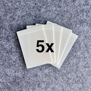 Peut inclure: Un ensemble de cinq cartes rectangulaires en plastique blanc dispos&eacute;es en &eacute;ventail. Les cartes ont une finition lisse et opaque avec une surface plane et propre. Le texte 5x est imprim&eacute; en police noire grasse au centre de la carte sup&eacute;rieure.