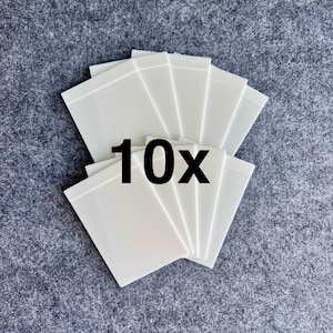 Peut inclure: Un ensemble de dix cartes rectangulaires en plastique blanc dispos&eacute;es en &eacute;ventail. Chaque carte pr&eacute;sente une surface lisse et opaque avec un design aux bords nets. Le texte noir en gras "10x" est centr&eacute; sur les cartes superpos&eacute;es.