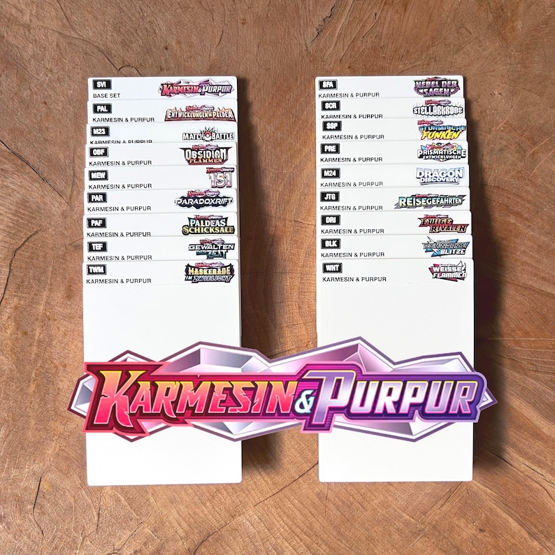 Peut inclure: Deux s&eacute;parateurs rectangulaires blancs pour cartes &agrave; collectionner, chacun pr&eacute;sentant une liste d'abr&eacute;viations et de logos de s&eacute;ries. Le grand logo en bas indique Karmesin & Purpur. Le texte inclut divers noms de s&eacute;ries comme Base Set, 151 et Paradox Rift.