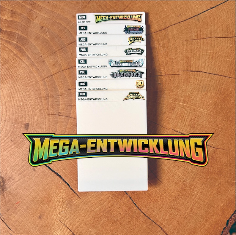 May include: A stack of white rectangular cards featuring the text Mega-Entwicklung and various expansion titles including Base Set, Fatale Flammen, Erhabene Helden, Optimale Ordnung, Wachsendes Chaos, Dunkelnacht, 30 Jahre, and Delta Herrschaft.
