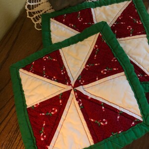 May include: Two red and white quilted pot holders with a candy cane pattern and green trim.