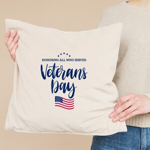 Puede incluir: Una almohada blanca con el texto "Honoring all who served Veterans Day" en letras azules y un gr&aacute;fico de la bandera estadounidense.
