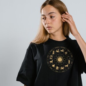 Op de afbeelding: Een zwart T-shirt met een gouden zodiac-wielontwerp met alle 12 astrologische tekens.