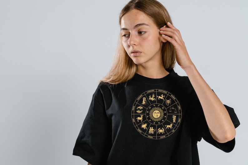 Op de afbeelding: Een zwart T-shirt met een gouden zodiac-wielontwerp met alle 12 astrologische tekens.