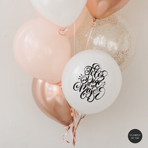 May include: A bunch of balloons in white, peach, and rose gold with a white balloon that says "Feliz Dia de la Mujer" in black calligraphy.
