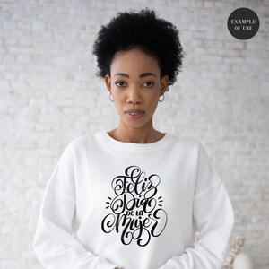 May include: White sweatshirt with black lettering that says "Feliz Dia de la Mujer" which translates to "Happy Women's Day" in English.