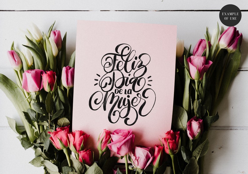 May include: A pink card with black calligraphy that reads "Feliz Dia de la Mujer" surrounded by pink and white tulips and roses.