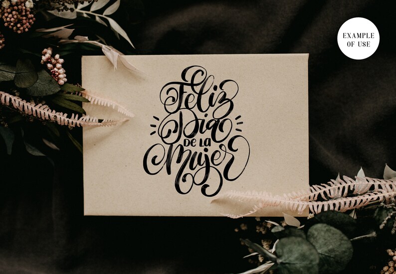 May include: A brown card with the text "Feliz Dia de la Mujer" written in black calligraphy.
