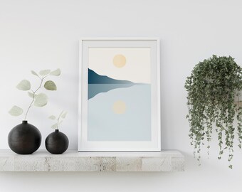 May include: A white framed print with a minimalist landscape design. The print features a blue mountain range reflected in a body of water with two yellow suns in the sky. The print is displayed on a white shelf with two black vases and a trailing green plant.