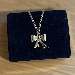 May include: A gold chain necklace with a gold bow pendant featuring a red gemstone in the center.
