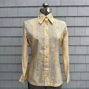May include: A long-sleeved, cream-colored blouse with a black and white geometric pattern. The blouse has a button-up front and a collared neckline.