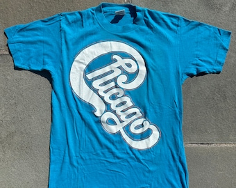 May include: A blue t-shirt with a white graphic of the word "Chicago" in a stylized font.