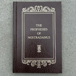 Pode incluir: Um livro encadernado em couro marrom com letras douradas na capa. O título é "The Prophesies of Nostradamus".