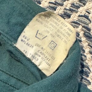 May include: Close-up of a teal fabric with a white tag. The tag includes washing instructions and warnings, such as "FLAMMABLE KEEP AWAY FROM SOURCE OF FLAME." The tag also has the text "RDU WPL6635".