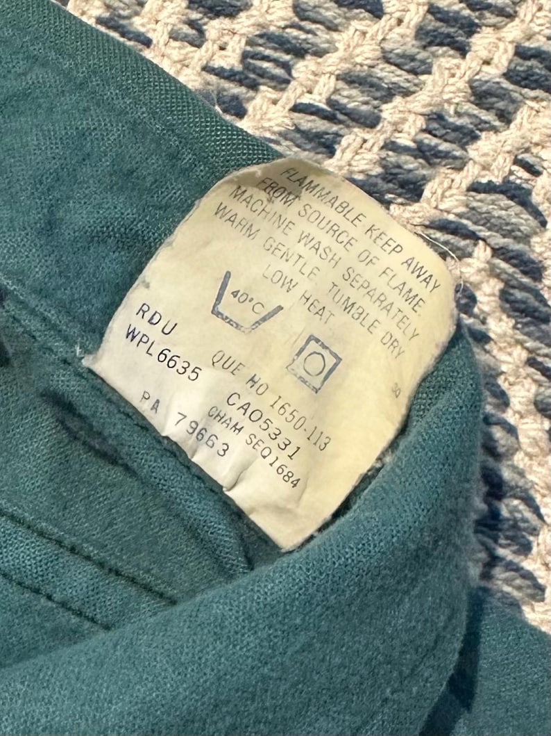 May include: Close-up of a teal fabric with a white tag. The tag includes washing instructions and warnings, such as "FLAMMABLE KEEP AWAY FROM SOURCE OF FLAME." The tag also has the text "RDU WPL6635".