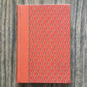 Puede incluir: Un libro de tapa dura rojo con un diseño estampado en negro y rojo. El libro tiene un lomo de color rojo sólido.