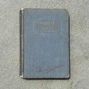 May include: A blue book with the title "Constipation: Its Cause, Effect and Treatment" written in gold lettering. The book has a handwritten signature on the front cover.