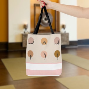 May include: A beige tote bag with black straps and a pink and white striped bottom. The bag features a pattern of yoga poses in brown and pink circles.