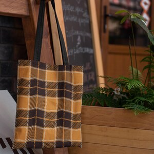 May include: A brown and yellow plaid tote bag with black straps hanging on a wooden rack.