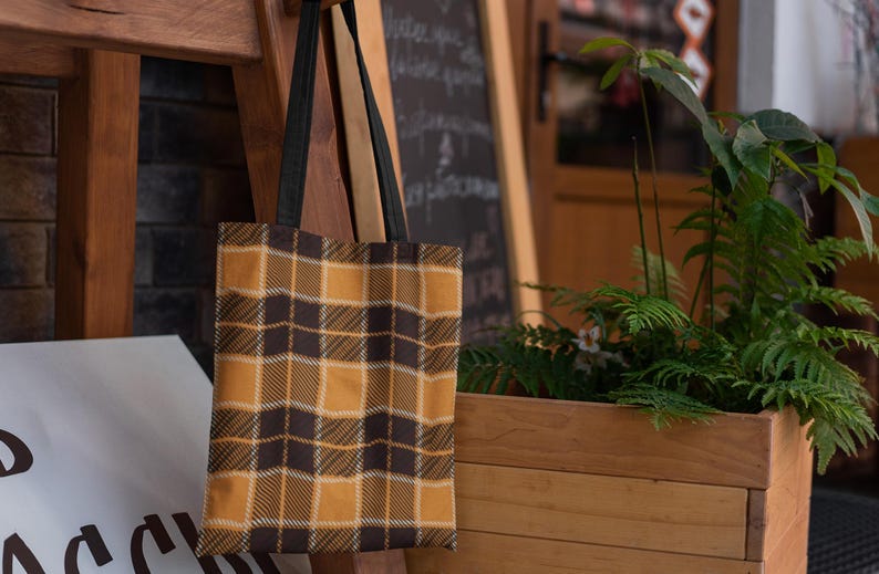 May include: A brown and yellow plaid tote bag with black straps hanging on a wooden rack.