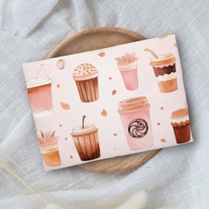 May include: A pink zippered pouch with a watercolor pattern of coffee cups and pastries. The pouch is on a wooden surface.