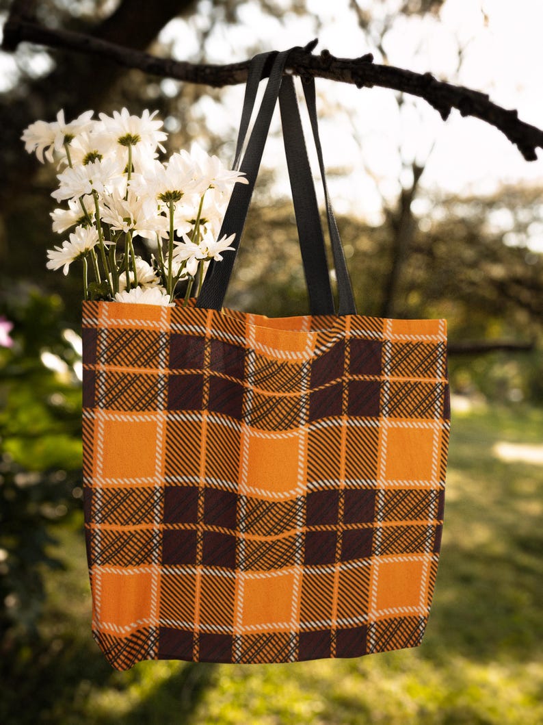 May include: A black and orange plaid tote bag with black straps hanging from a tree branch. White daisies are in the bag.