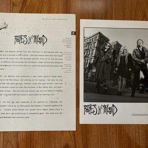 May include: Two vintage Babes in Toyland band promotional items. One is a black and white photo of the band in front of a building. The other is a media information sheet with text about the band.