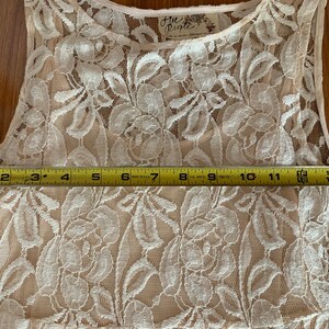 May include: A white lace sleeveless top with a Free People tag. The top is measured across the bust with a tape measure, showing a measurement of 15 inches.