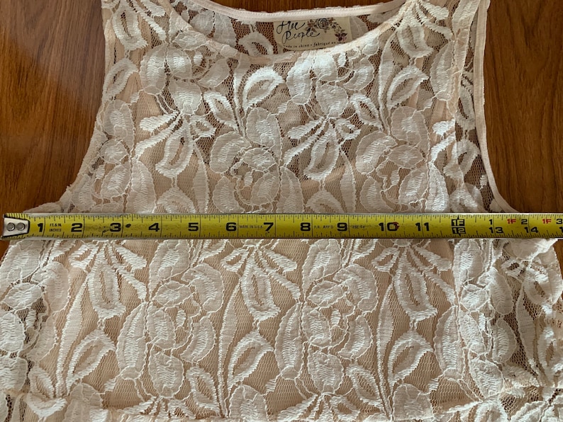 May include: A white lace sleeveless top with a Free People tag. The top is measured across the bust with a tape measure, showing a measurement of 15 inches.