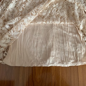 May include: A white lace skirt with a beige lining. The skirt is made of delicate lace with a floral pattern.