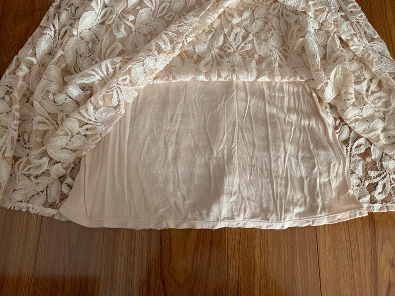 May include: A white lace skirt with a beige lining. The skirt is made of delicate lace with a floral pattern.