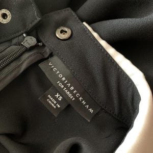 May include: Close-up of a black garment with a zipper and snap closures. The label reads "VICTORIA BECKHAM FOR TARGET" with "XS" size and "MADE IN CHINA" text.