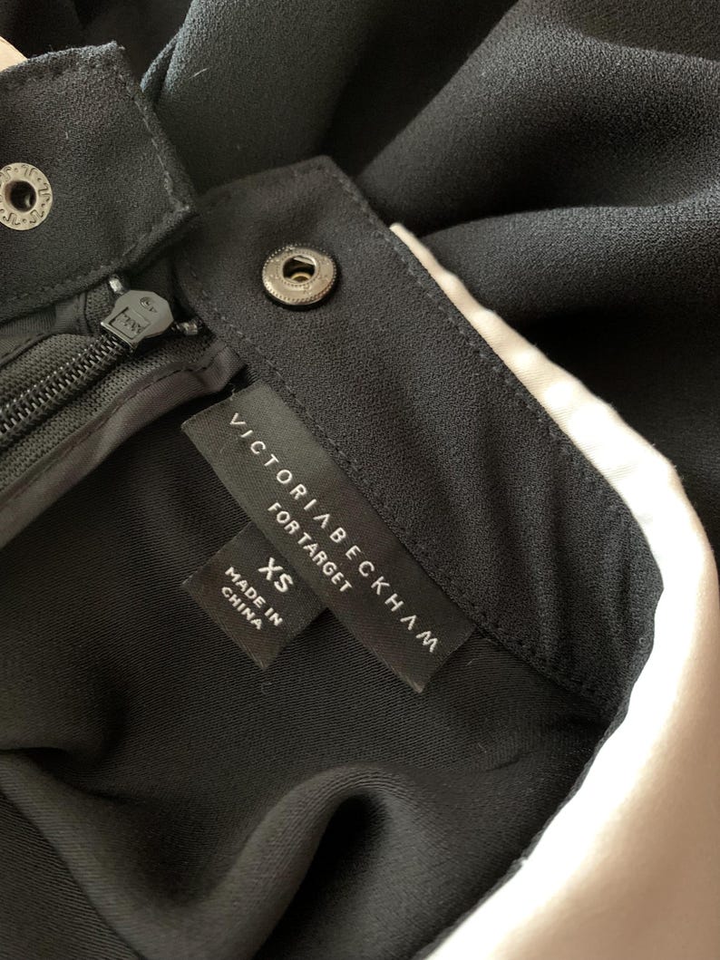May include: Close-up of a black garment with a zipper and snap closures. The label reads "VICTORIA BECKHAM FOR TARGET" with "XS" size and "MADE IN CHINA" text.
