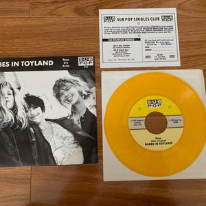 May include: A Babes in Toyland 7-inch vinyl record titled House b/w Arribe on a yellow disc with a black and white sleeve featuring three people. Includes a Sub Pop Singles Club insert with a schedule of releases and a mail-in subscription form.