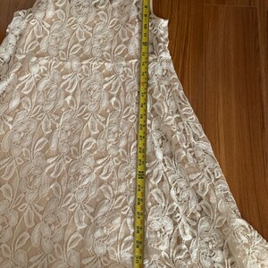 May include: A white lace dress with a floral pattern. The dress is sleeveless and has a scoop neck. It is approximately 33 inches long.