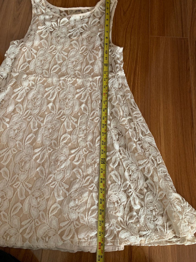 May include: A white lace dress with a floral pattern. The dress is sleeveless and has a scoop neck. It is approximately 33 inches long.