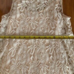 May include: A white lace sleeveless top with a floral pattern. The top is measured to be 18 inches wide.