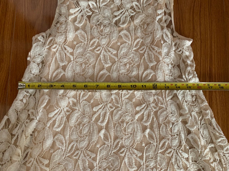 May include: A white lace sleeveless top with a floral pattern. The top is measured to be 18 inches wide.