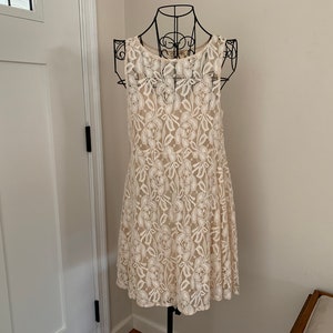 May include: A white lace dress with a floral pattern. The dress is sleeveless and has a round neckline.