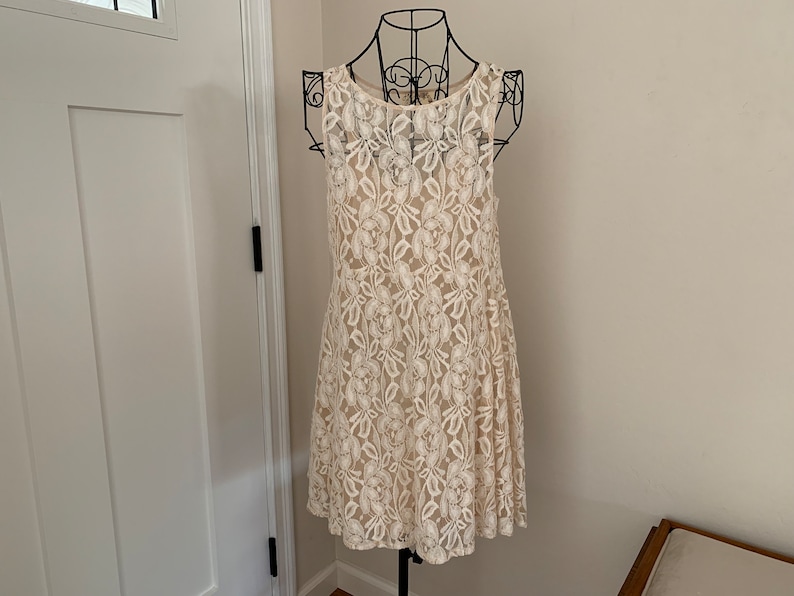 May include: A white lace dress with a floral pattern. The dress is sleeveless and has a round neckline.