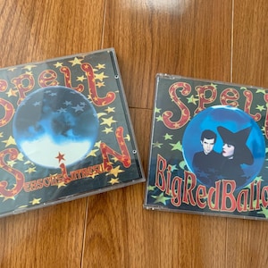 May include: Two CD cases with album art. One case has a blue sphere with stars and the text "Spell" and "Seasons of the Withes". The other case has a blue sphere with two people and the text "Spell" and "Big Red Balloon".