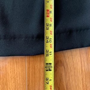 May include: A black garment is measured with a yellow measuring tape. The tape shows a length of 30 to 37 inches. The garment is on a wooden surface.