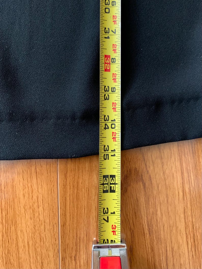 May include: A black garment is measured with a yellow measuring tape. The tape shows a length of 30 to 37 inches. The garment is on a wooden surface.